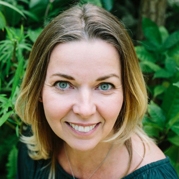 Woman with shoulder-length blonde hair smiling in a garden setting.